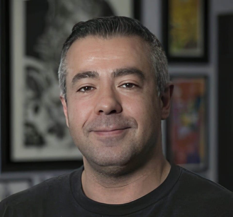 Leo Cadenazzi smiles in front of framed tattoo artwork.