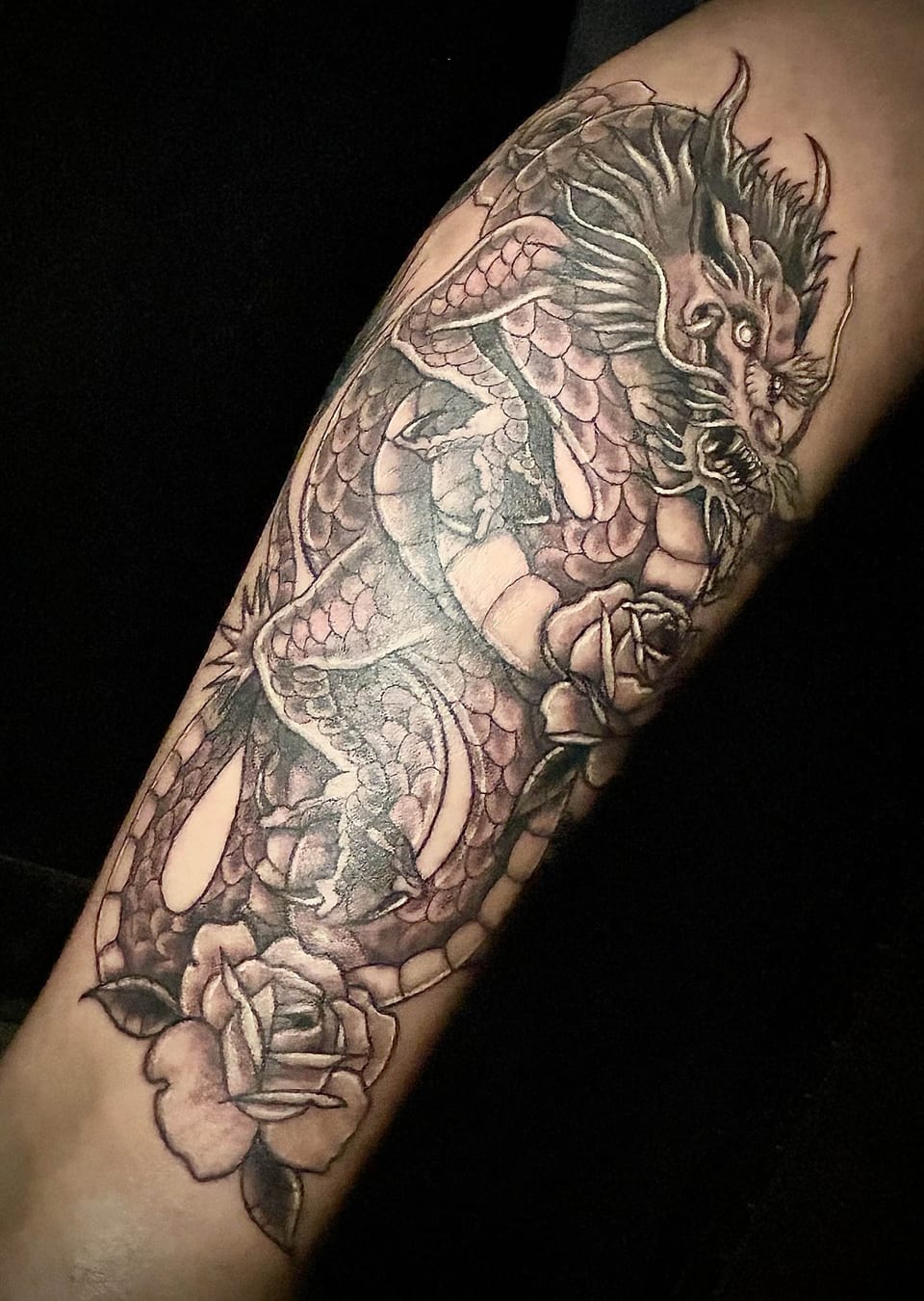 A black and grey Japanese dragon coils among flowers and rocks on the arm.