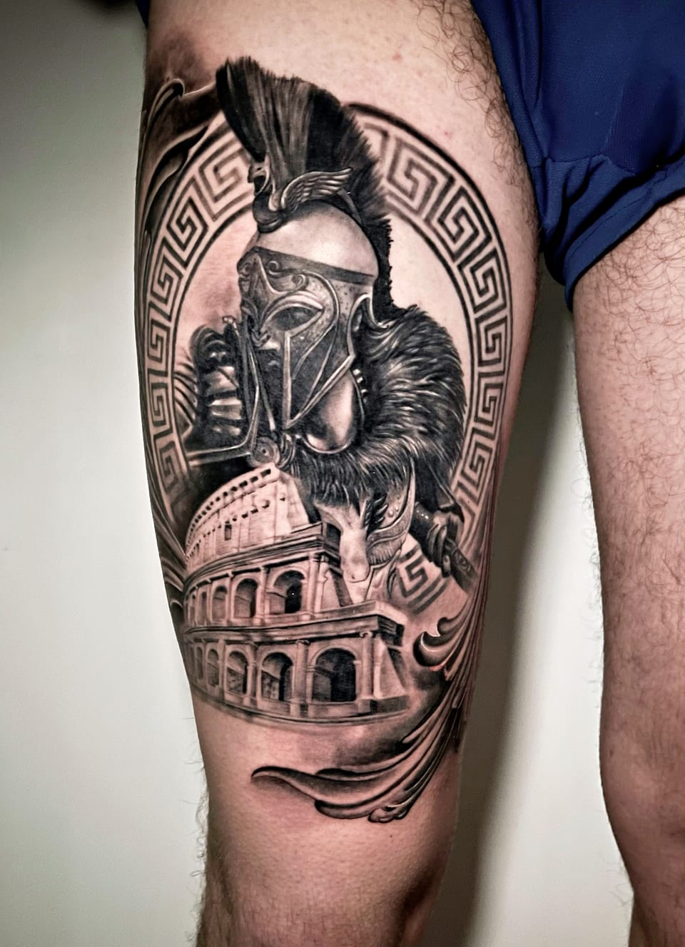 A black and grey realism warrior helmet and amphitheater fill a thigh.