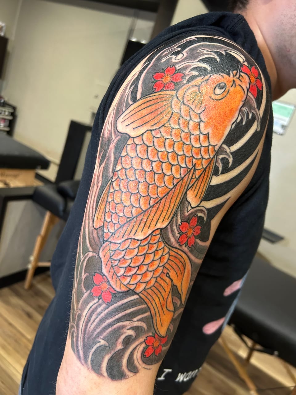 Japanese color orange koi with waves and red blossoms covers the upper arm.