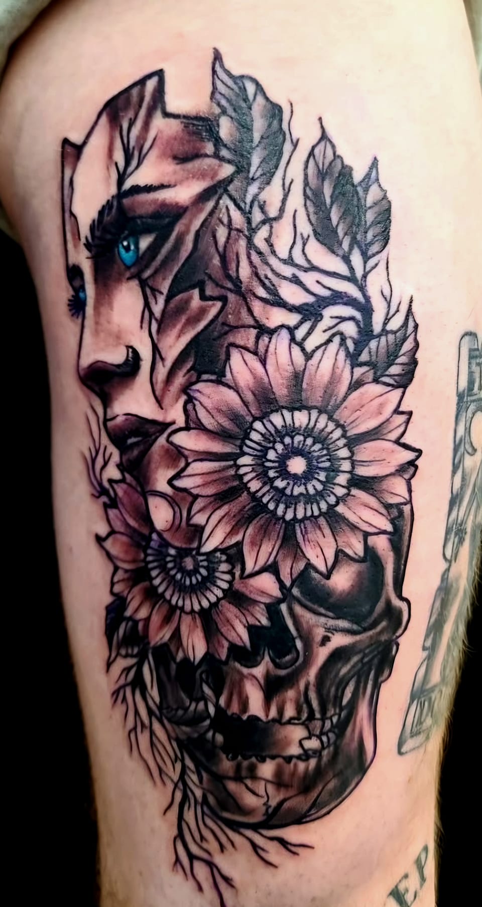 A woman, flowers and a skull form a black and grey forearm tattoo.