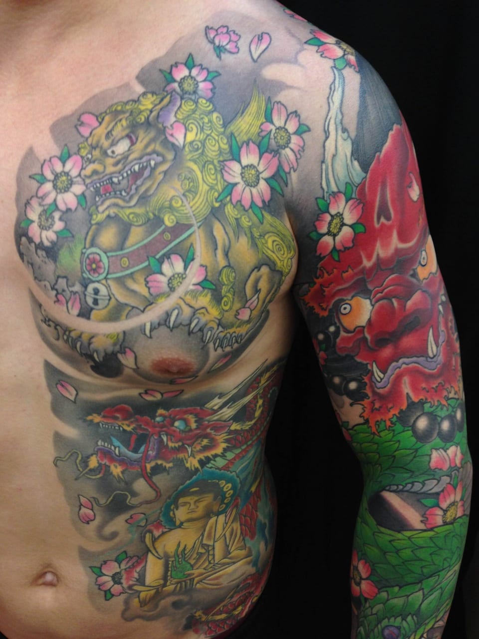 A colorful Japanese tattoo with a foo dog, dragons, Buddha and blossoms covers the chest, torso and arm.