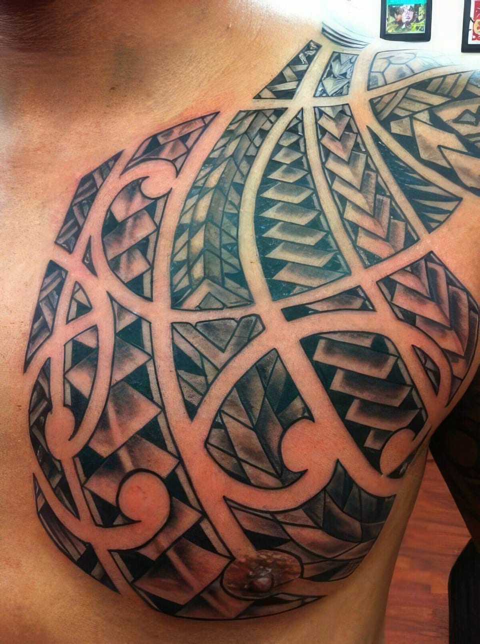 Black Polynesian-style spiral and geometric patterns tattooed on a chest and shoulder, tattooed by Seth Reynolds