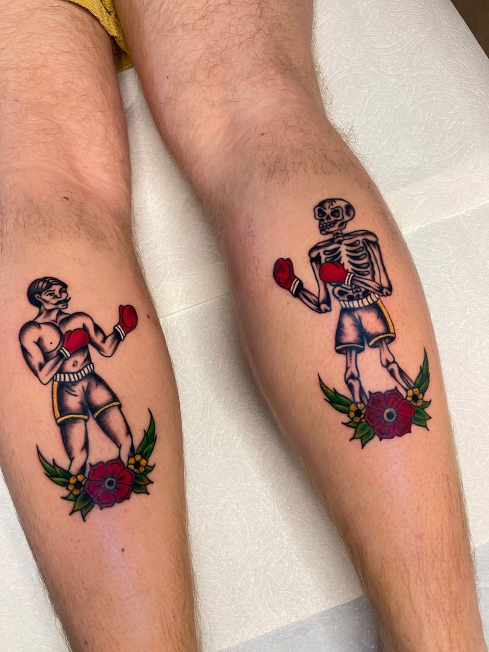 Color traditional boxers, one a skeleton, stand above red roses on a pair of lower legs.